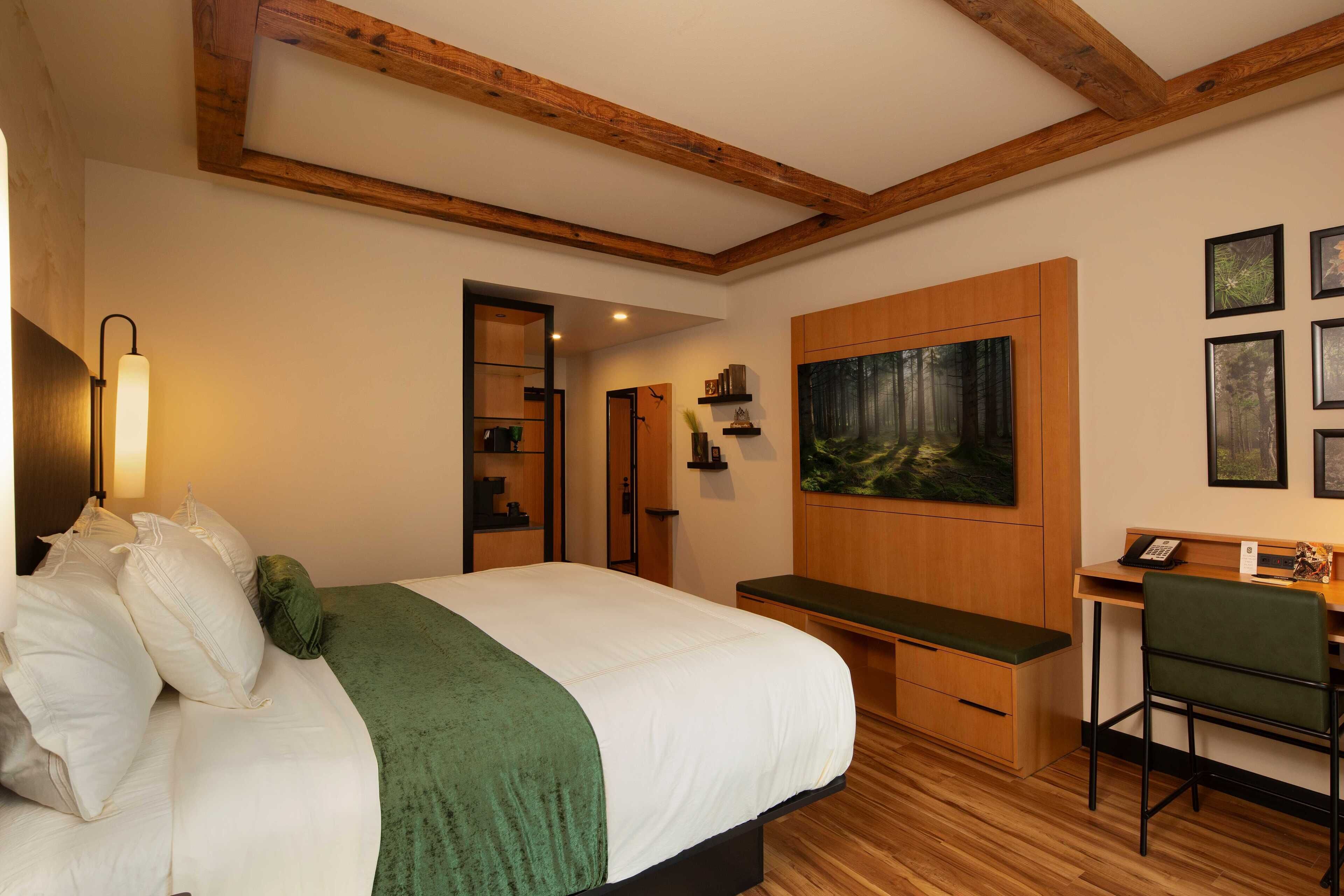 Une chambre à coucher avec un lit, un bureau, une chaise, un tableau et un plafond en bois.