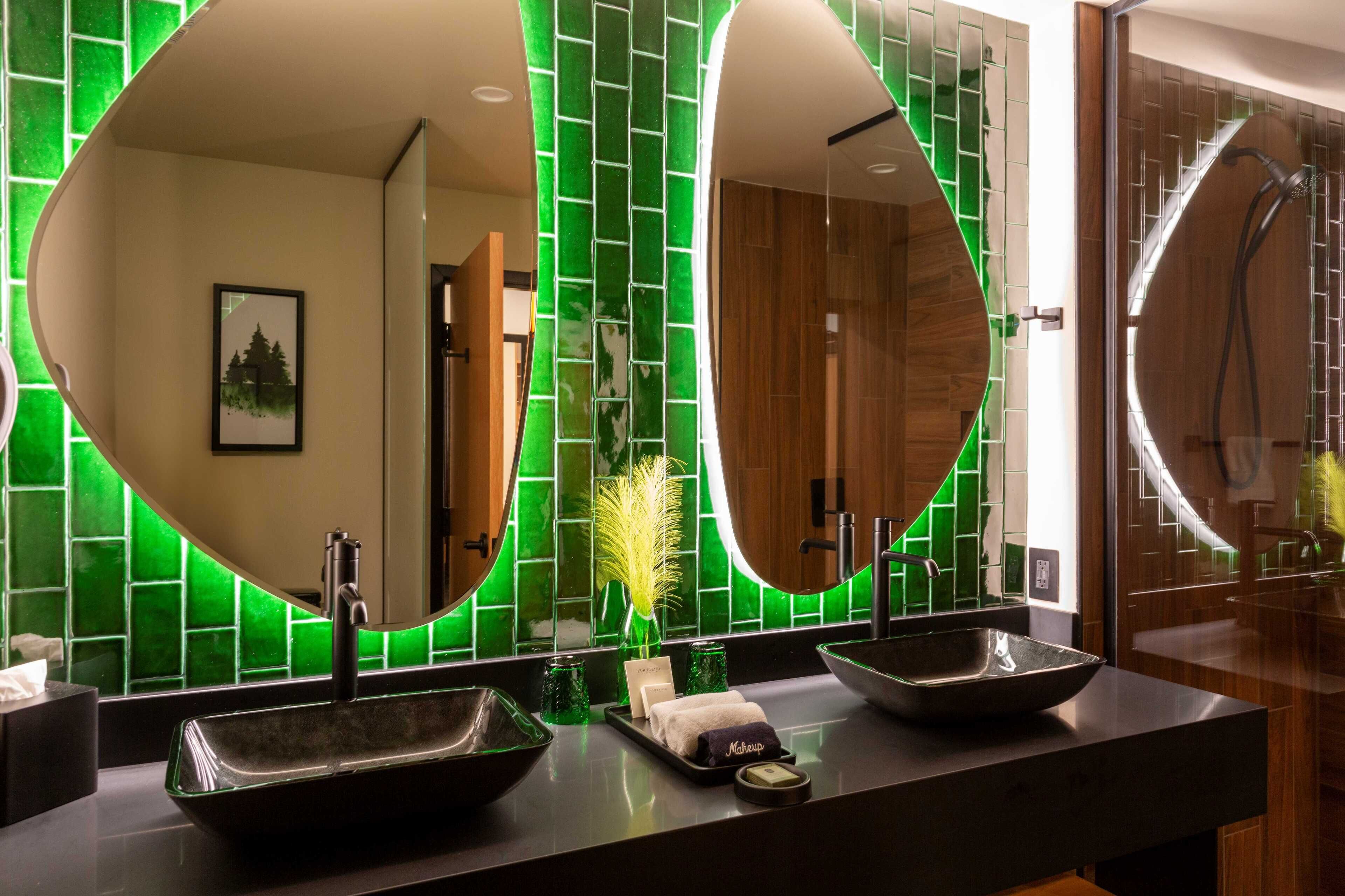 Un baño moderno con dos espejos ovalados grandes, un lavabo negro y una zona de ducha.