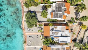 Vista aérea de una propiedad costera con playa, varias edificaciones y palmeras.