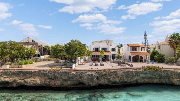 Una propiedad costera con piscina, mobiliario exterior y un litoral rocoso.