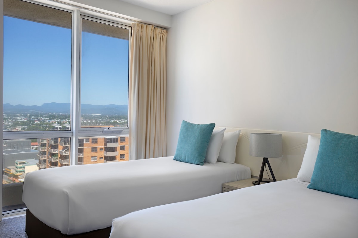 Une chambre d’hôtel avec deux lits, une grande fenêtre et une vue sur le paysage urbain.