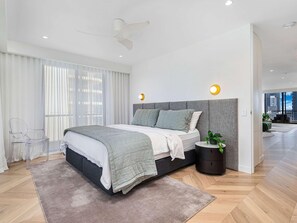 Quarto moderno com cama, mesa de cabeceira e vista da cidade.