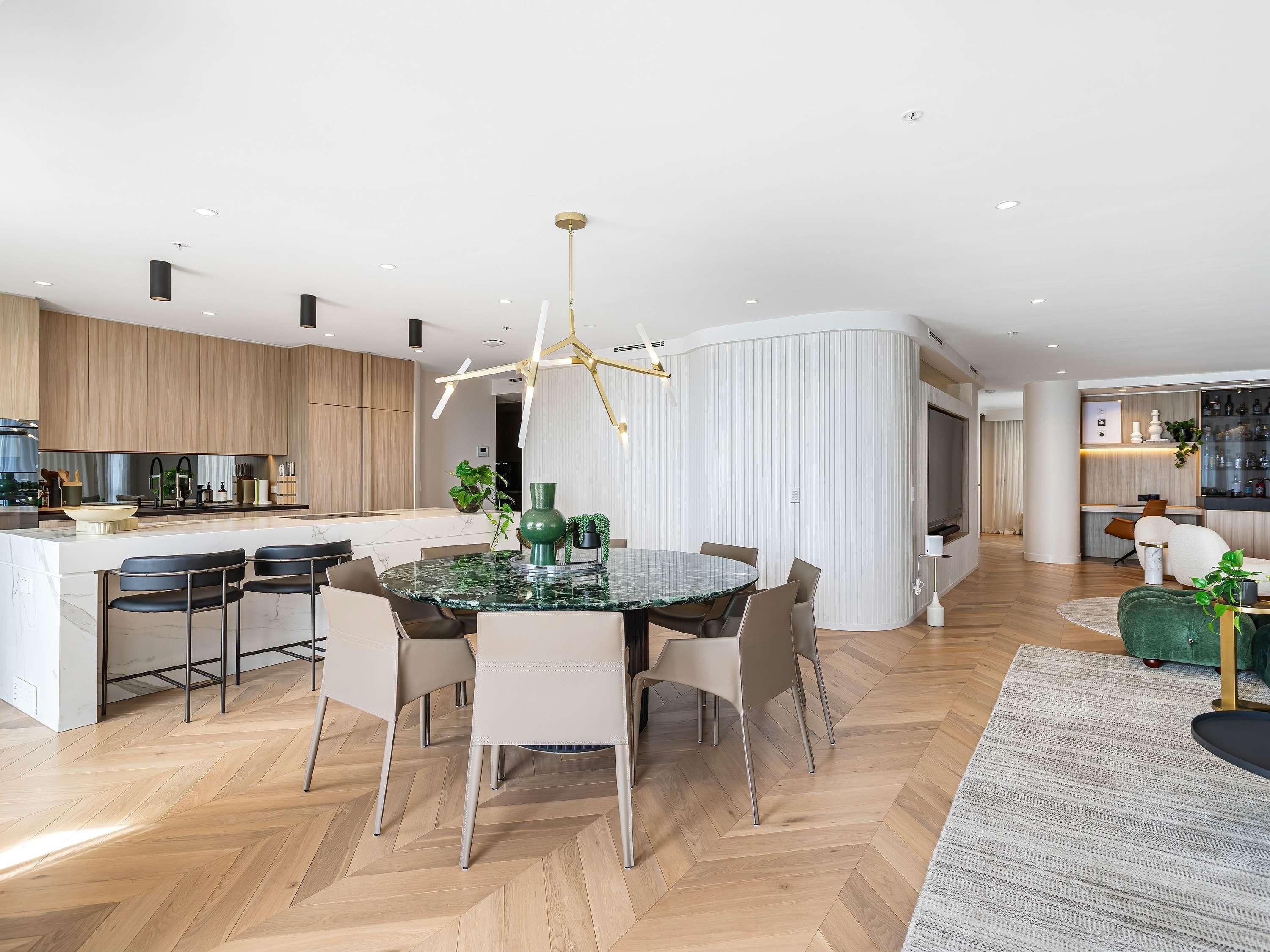 A modern kitchen with a central island, a dining area with a glass table, and a living space with a sofa and a TV.