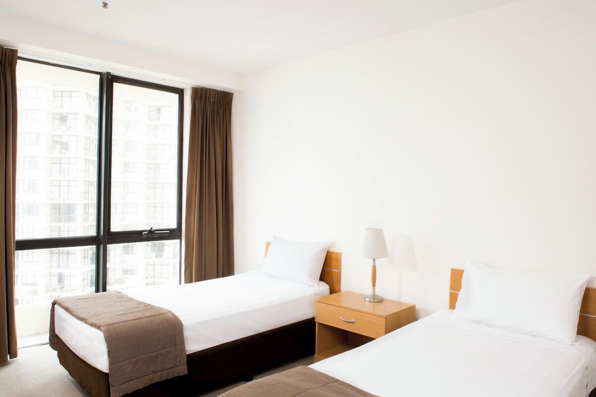 Une chambre d’hôtel avec deux lits, une fenêtre avec des rideaux et une table de chevet avec une lampe.