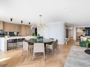 A modern kitchen with a central island, a dining area with a glass table, and a living space with a sofa and a TV.