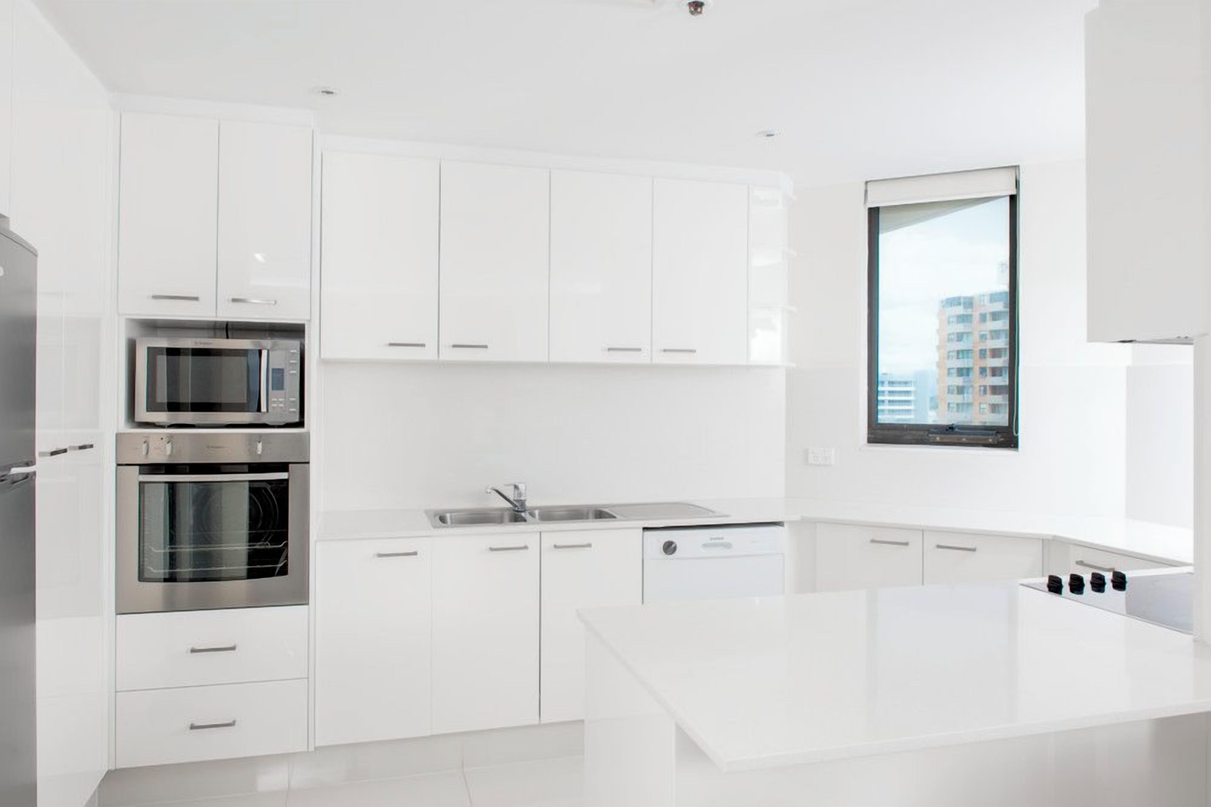 Una cocina moderna con armarios blancos, microondas integrado, horno y pileta.