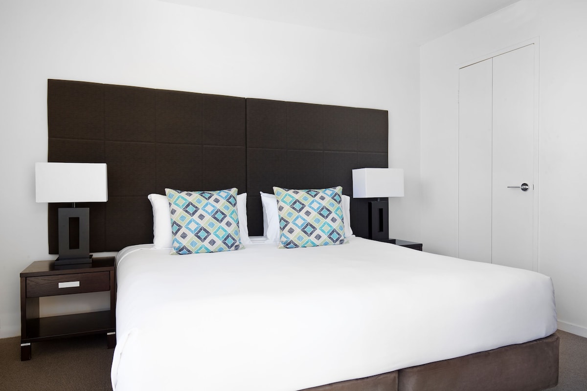 Une chambre d’hôtel avec un grand lit, deux tables de chevet avec des lampes et une porte blanche.