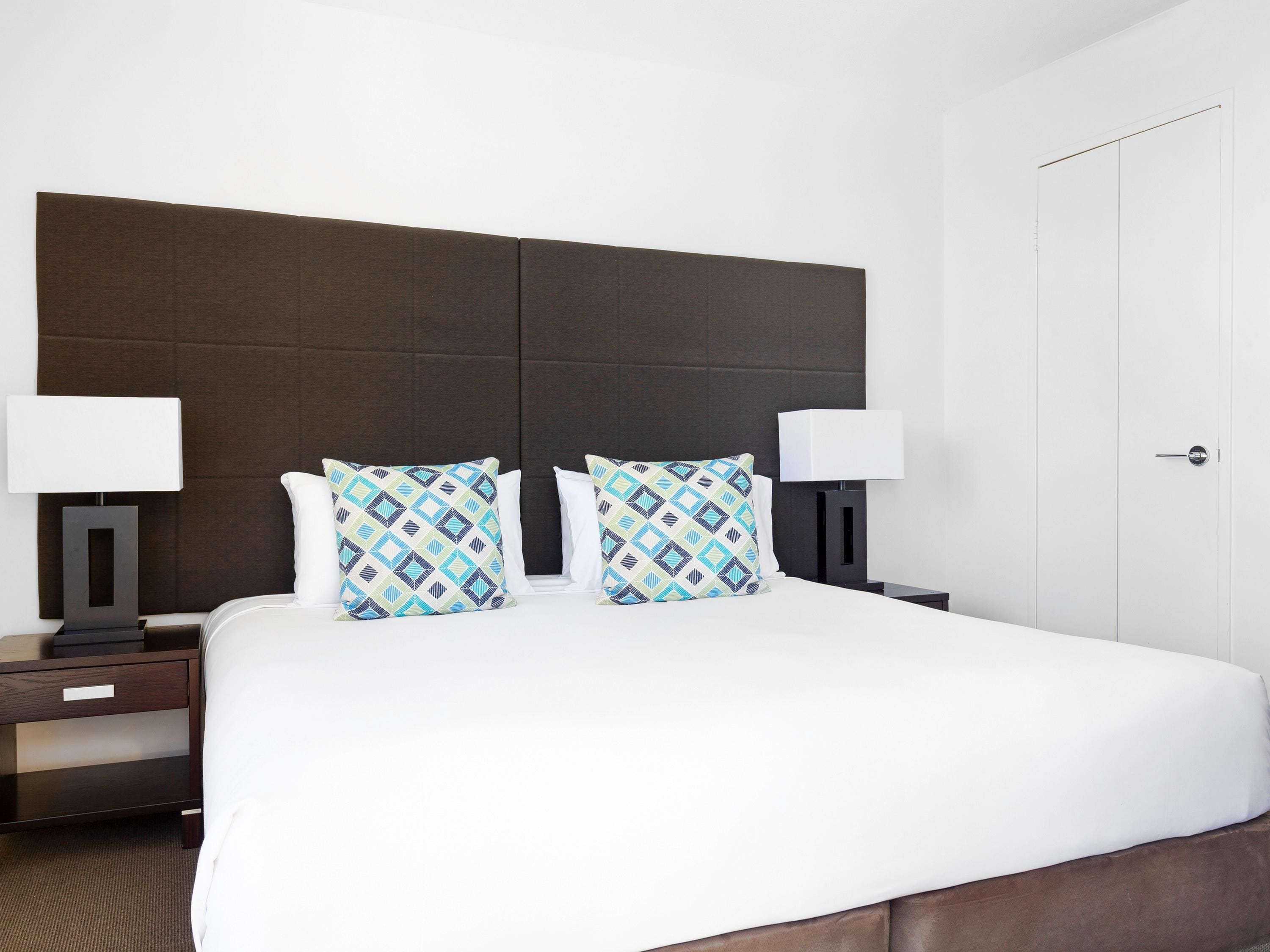 Una habitación de hotel con una cama grande, dos mesitas de noche y un armario.