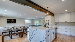 A modern kitchen with a marble island, wooden flooring, and white cabinetry. - Large Group Getaway | Hot Tub, Games & Pickleball (American Fork)