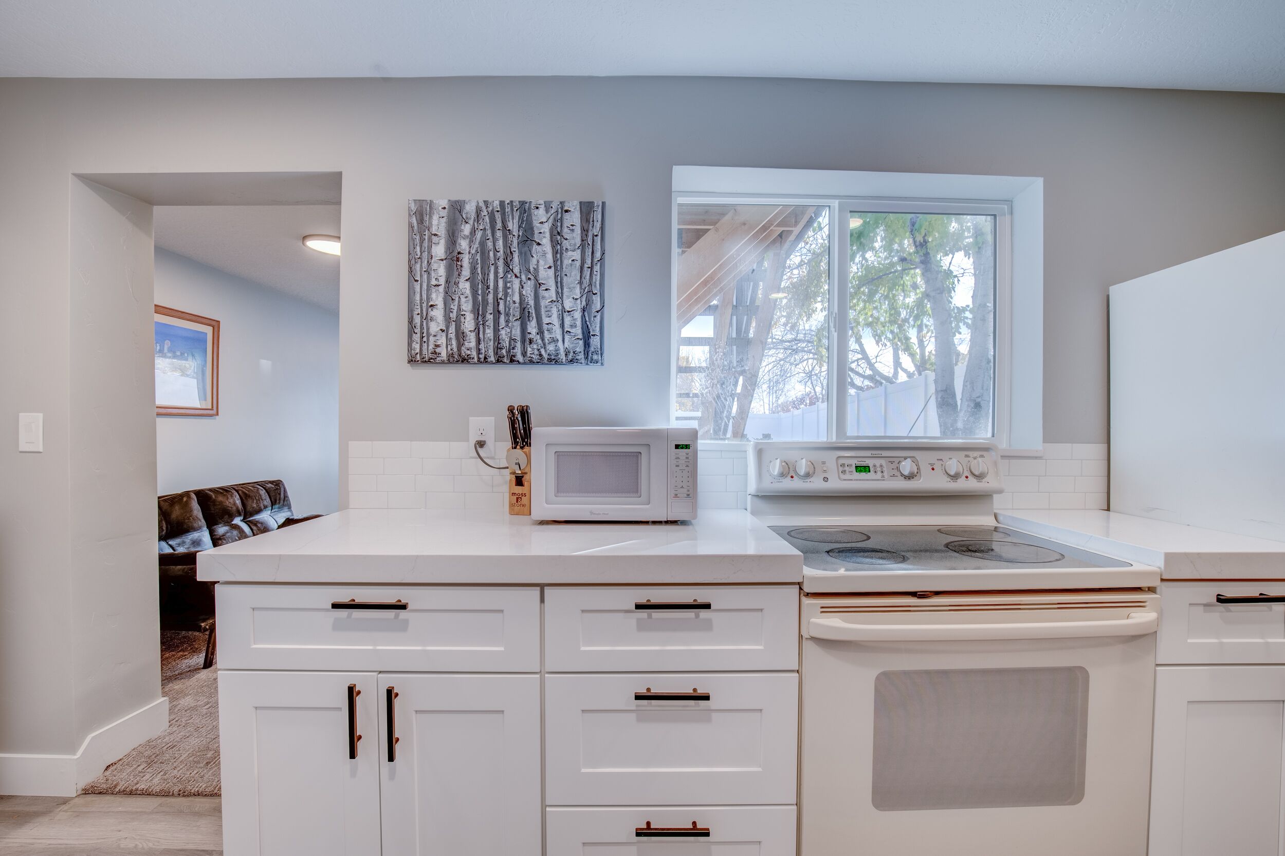 A modern kitchen with white cabinets, a microwave, an oven, and a window providing natural light.