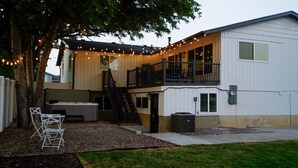 Une maison à deux étages dotée d’un balcon, d’un espace salon extérieur et de guirlandes lumineuses.
