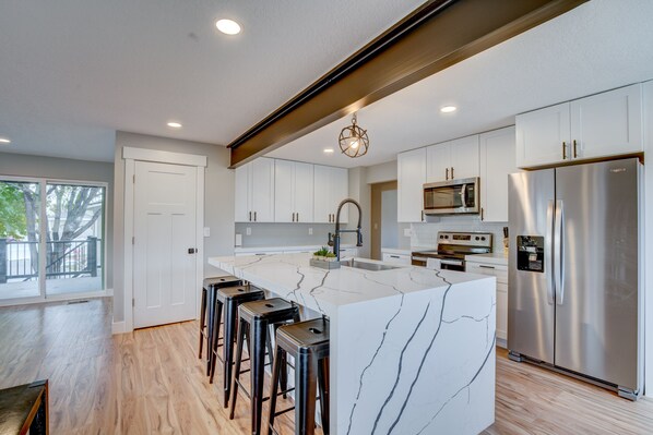 A modern kitchen with white cabinets, a marble island, stainless steel appliances, and a bar stool area.