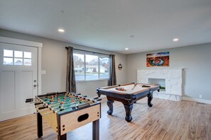 A room with a foosball table, pool table, and a fireplace.