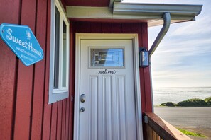 A red building with a white door labeled "Sweet Homes vacation getaways" and a "welcome" sign above it. - Ocean Front 5 BR Home! Yachats, Walk to Everything! Dog Friendly! (Yachats)