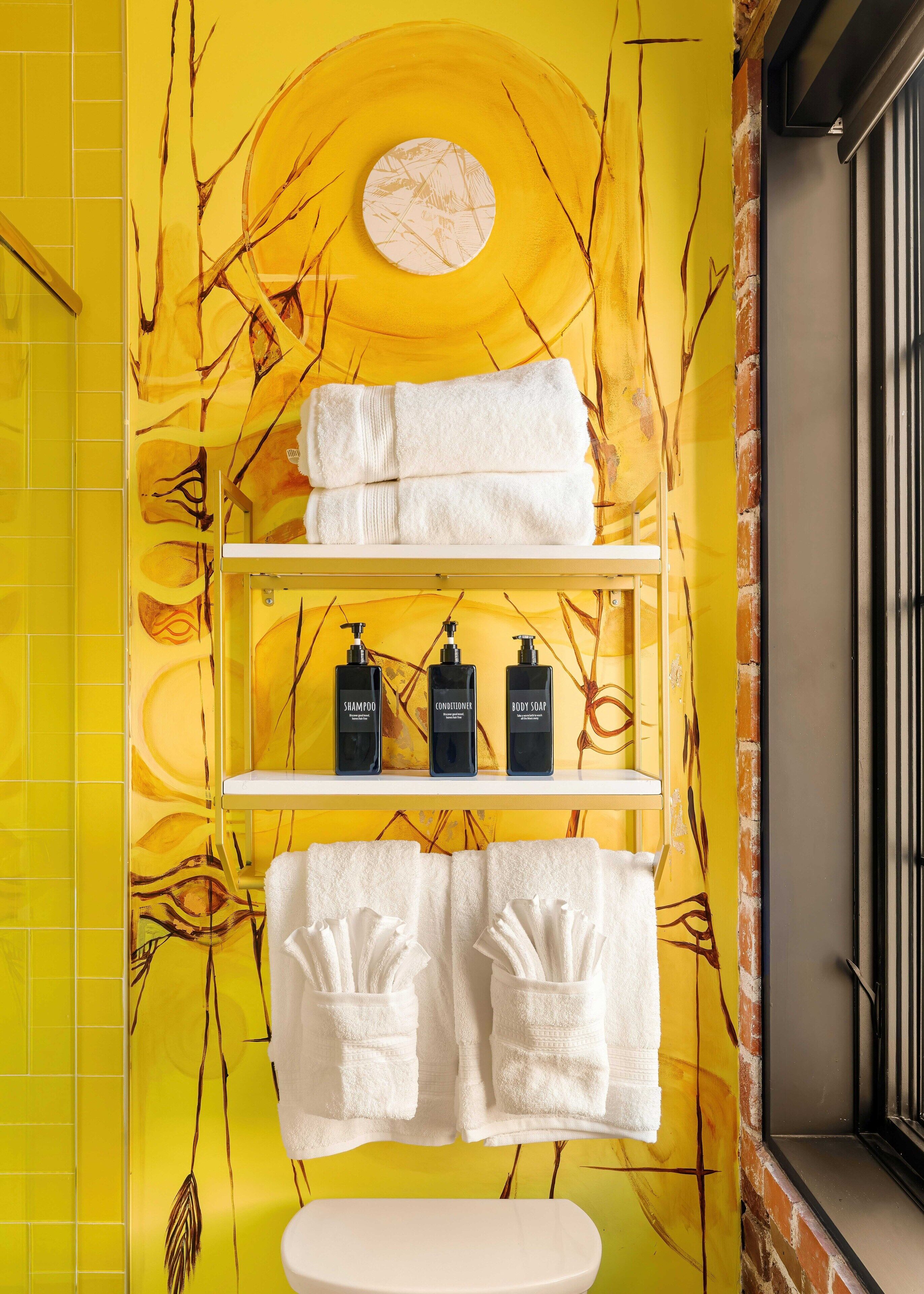 A bathroom with yellow walls, a white sink, and shelves holding towels and toiletries.