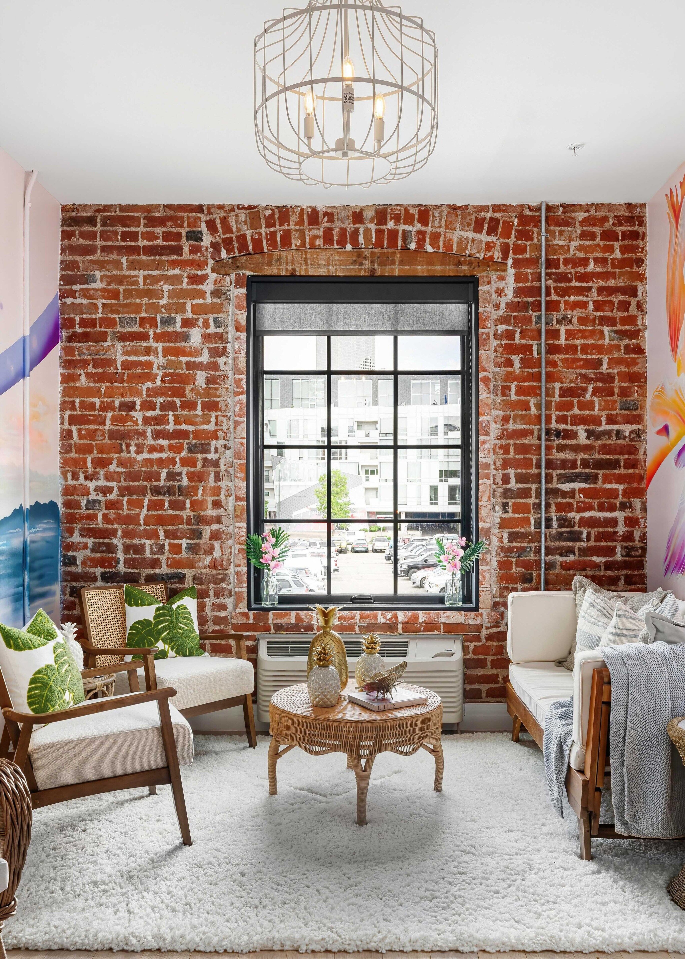 A cozy room with a brick wall, a large window, and a white ceiling fan.