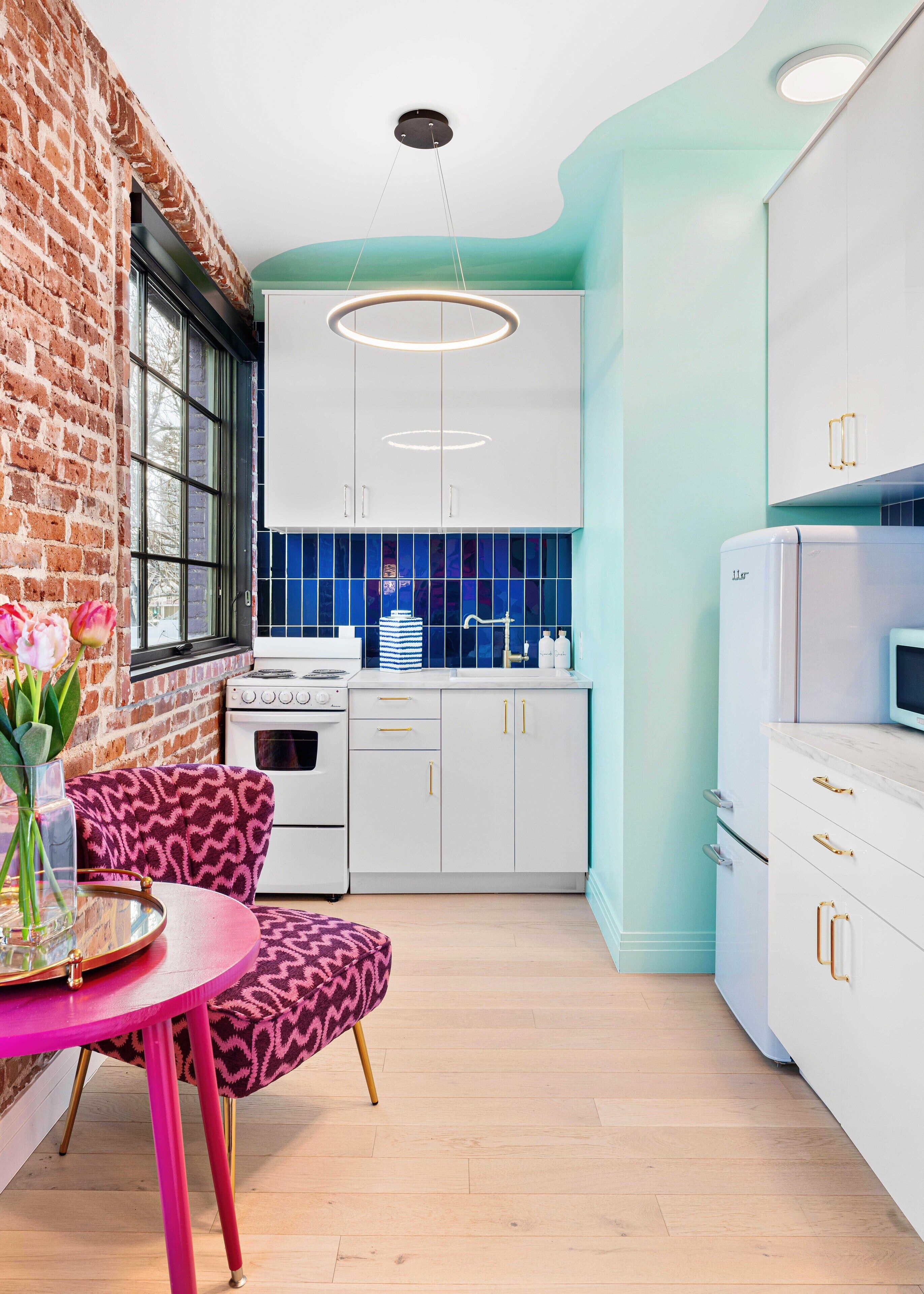 Una cocina moderna con armarios blancos, un salpicadero azul y una pared de ladrillo.
