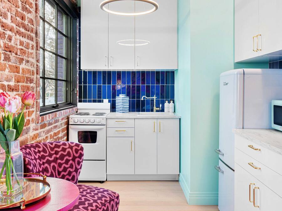 Una cocina moderna con armarios blancos, un salpicadero azul y una pared de ladrillo.