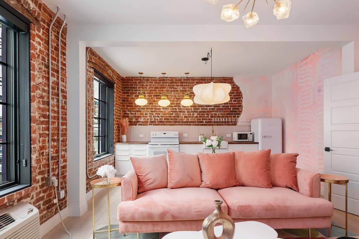 A modern living room with a pink sofa, a white coffee table, and a kitchen in the background.