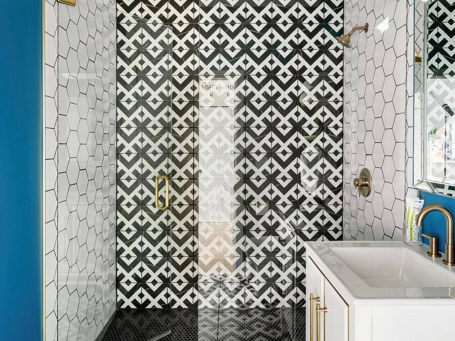 Un baño moderno con baldosas de diseño geométrico, cabina de ducha de vidrio y lavamanos blanco con detalles dorados.