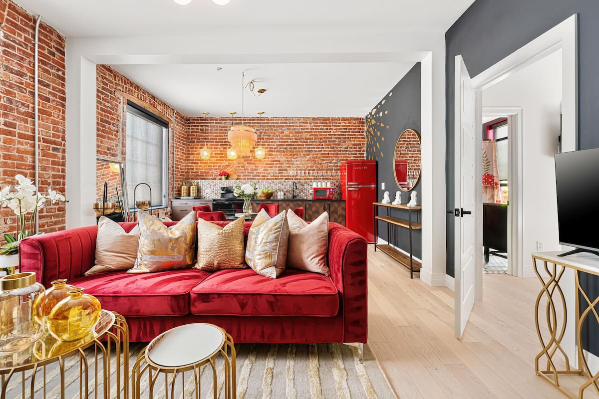 A modern living room with a red sofa, a dining area, and a kitchen with brick walls.