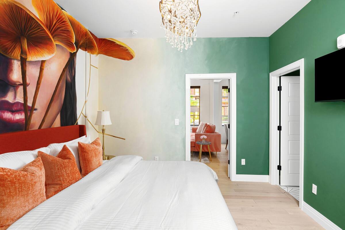 A bedroom with a large bed, a chandelier, a TV, and a green wall.