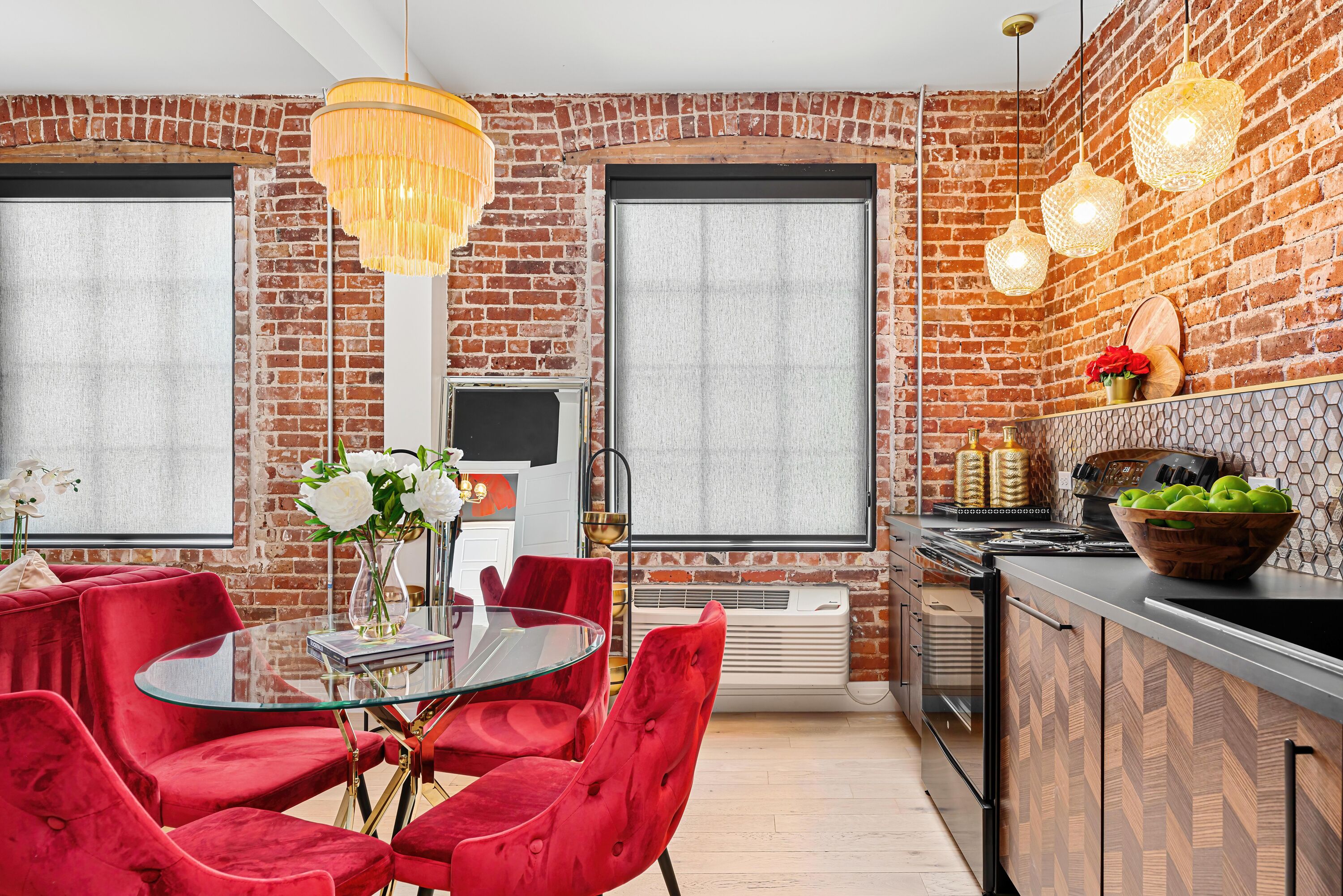 A modern kitchen with a brick wall, a dining area with red chairs, and a large window.