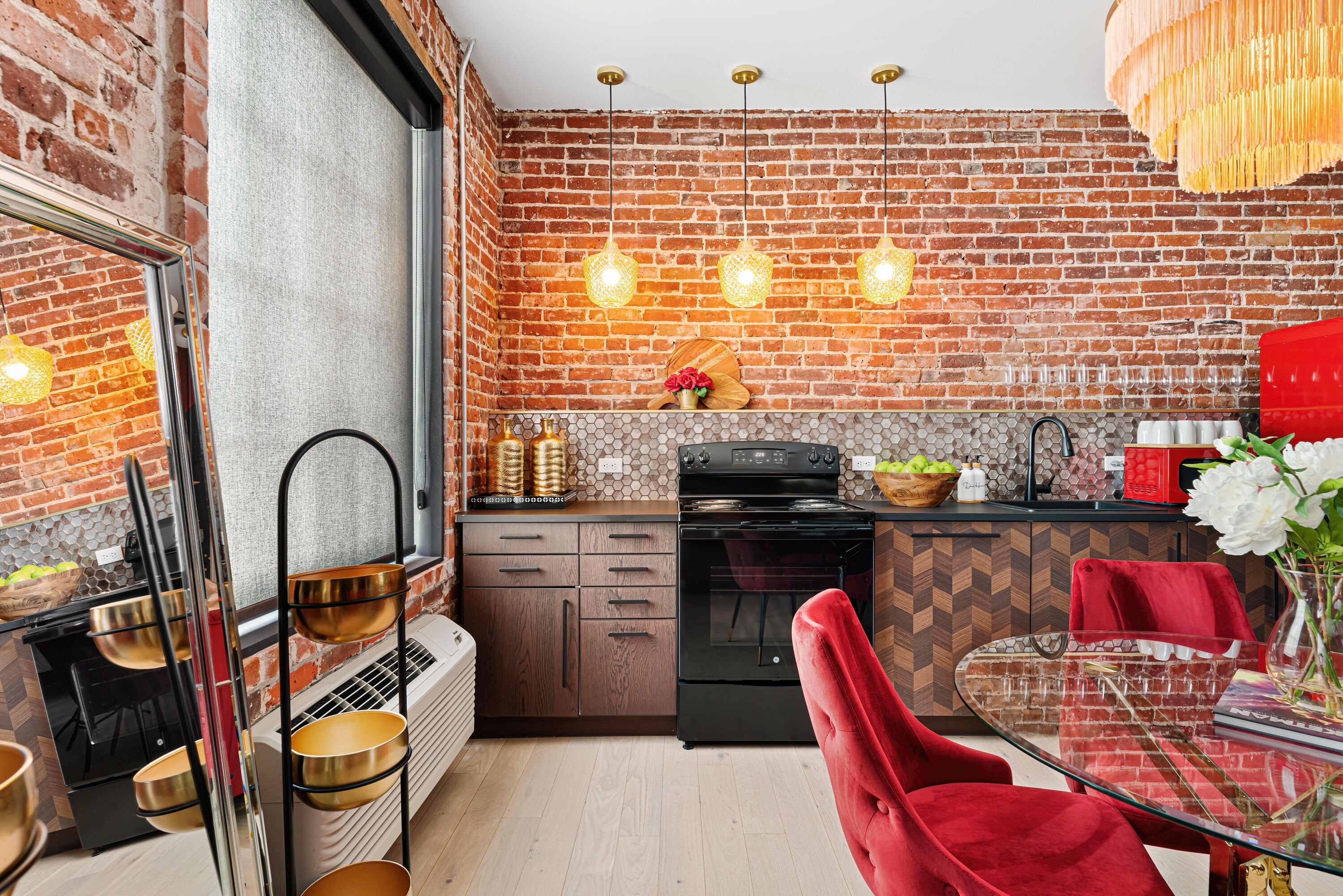 A kitchen with a brick wall, a black oven, and a glass dining table with red chairs.