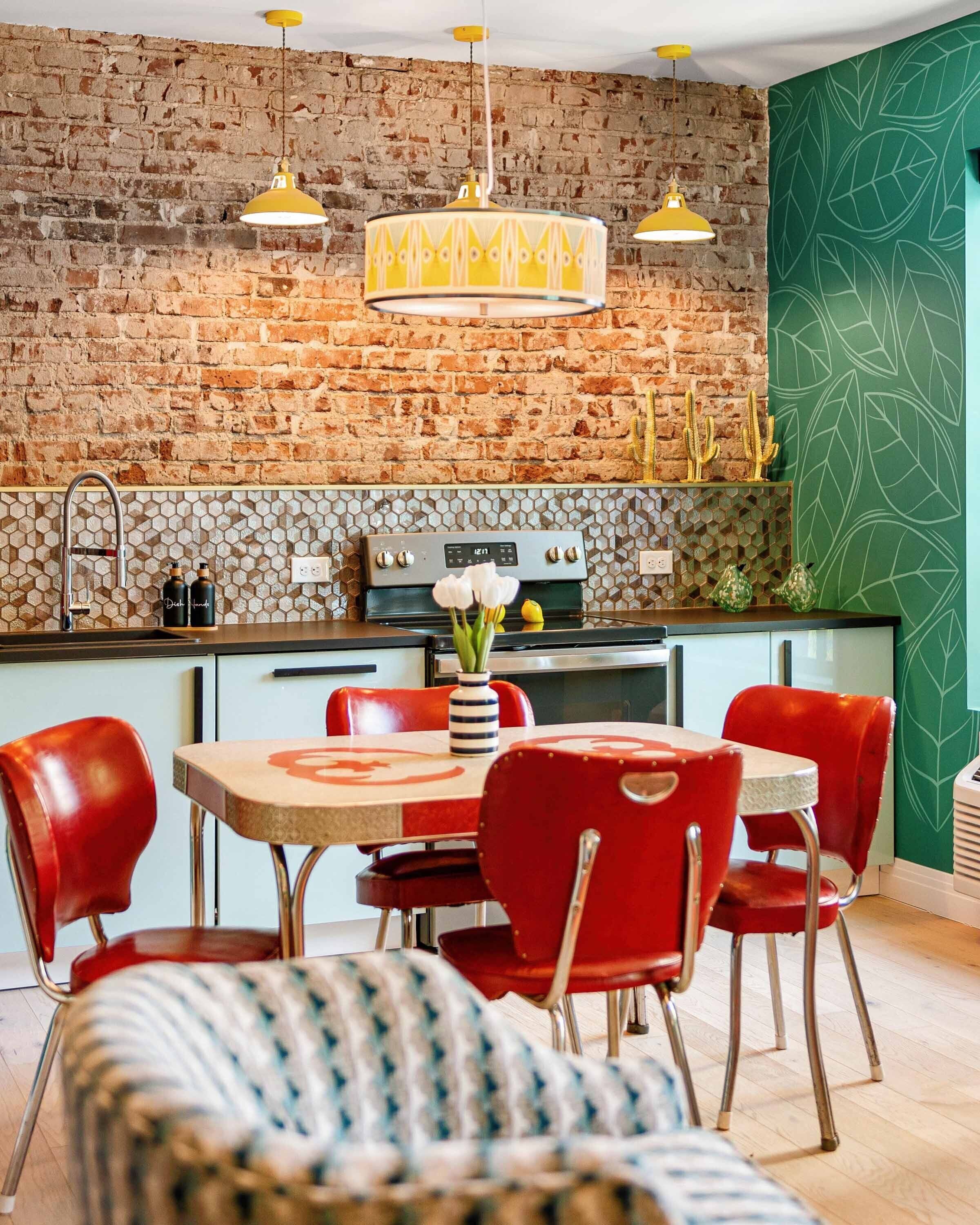 A kitchen with a brick wall, a dining table with red chairs, and pendant lights.