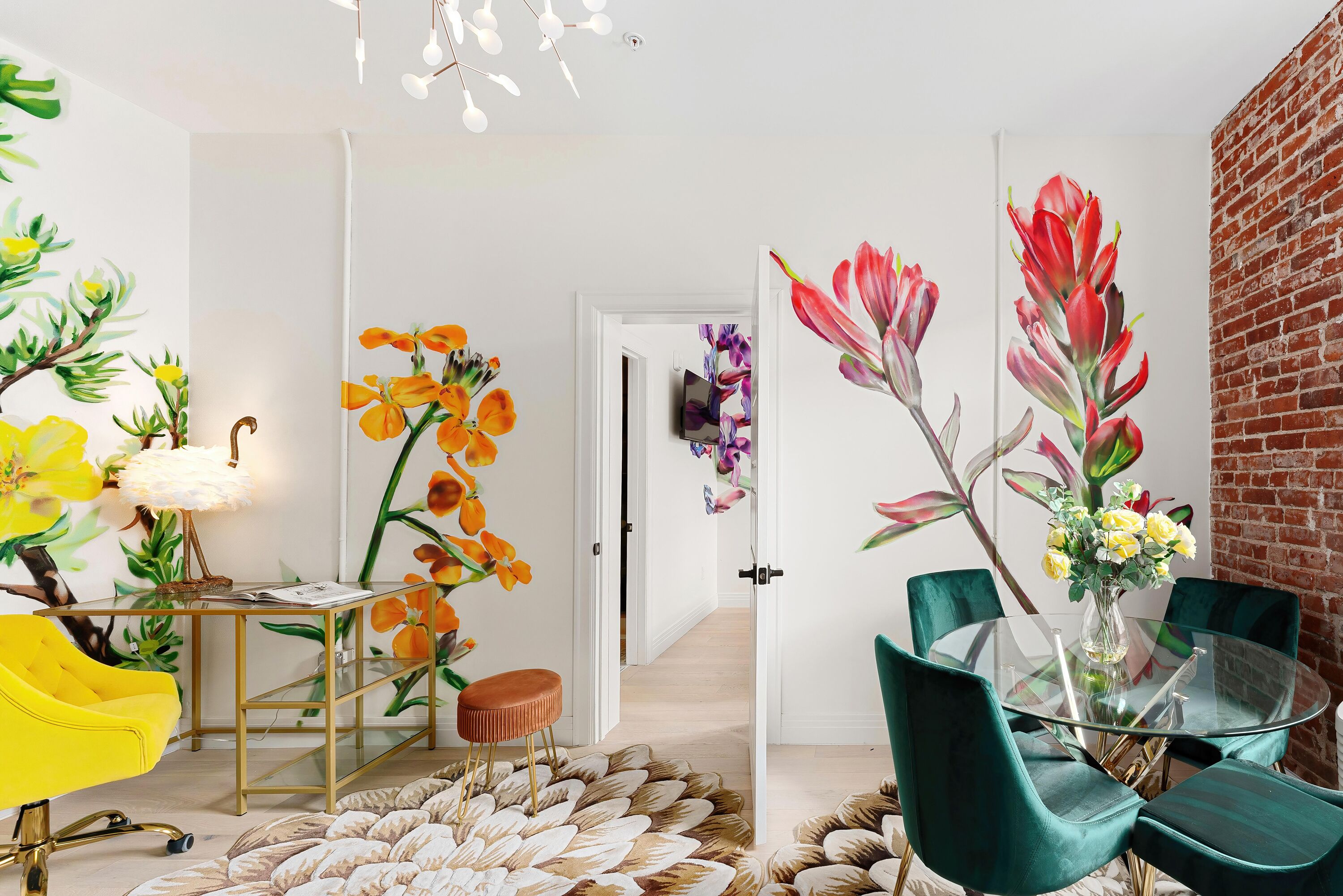 Uma área de refeições com mesa de vidro, cadeiras verdes e um vaso de flores.