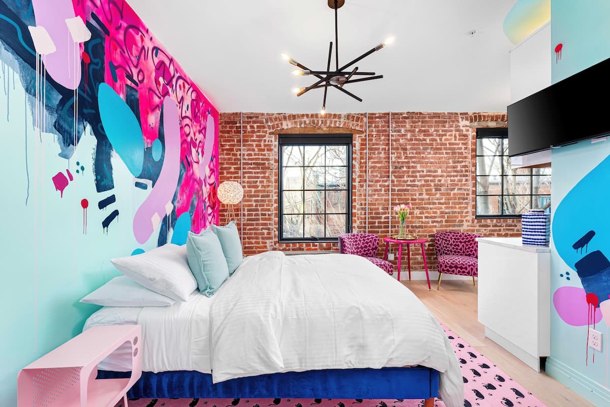 A bedroom with a brick wall, a large bed, a TV, and a window.