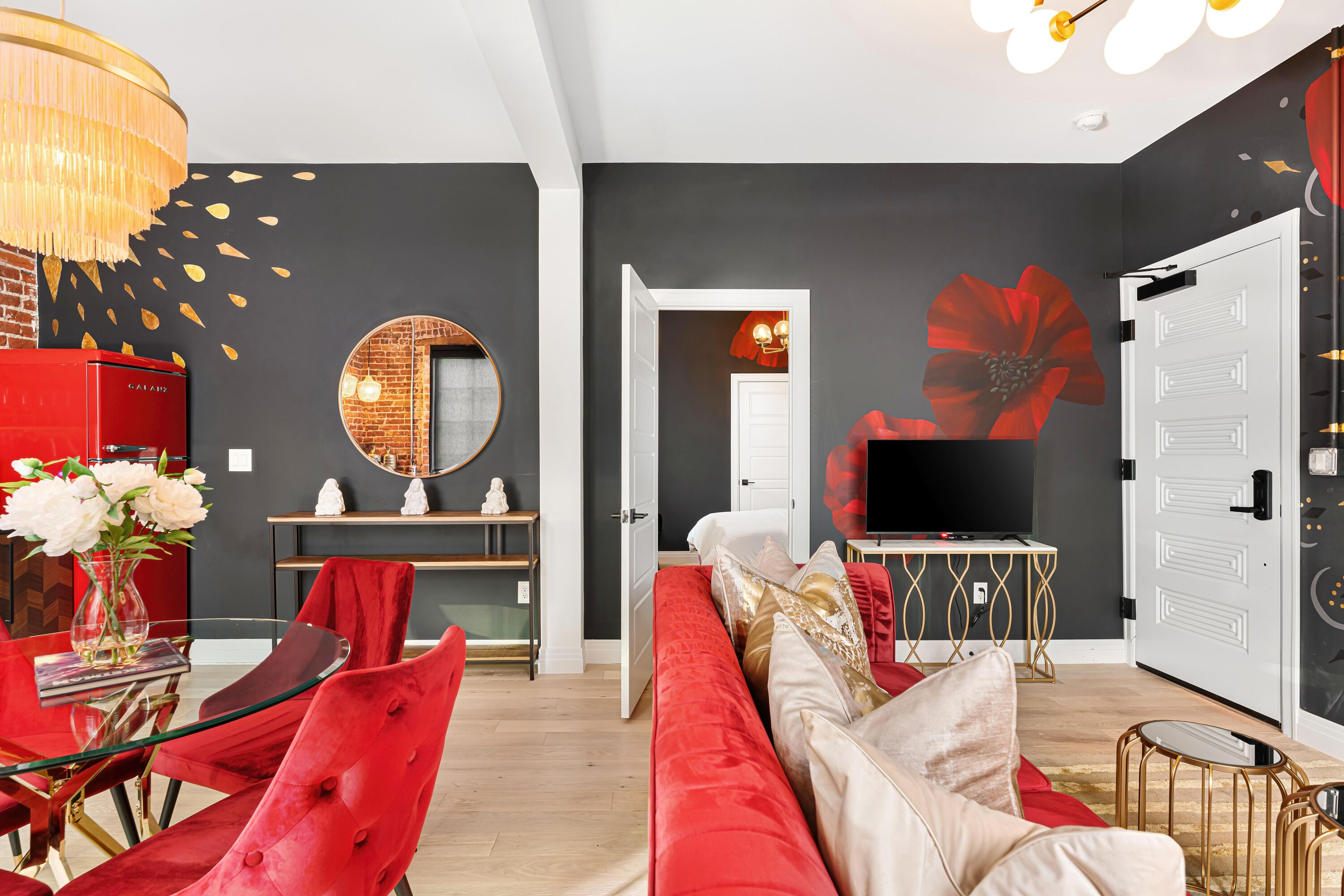 A modern living room with a red sofa, a glass coffee table, and a TV on a gold stand.