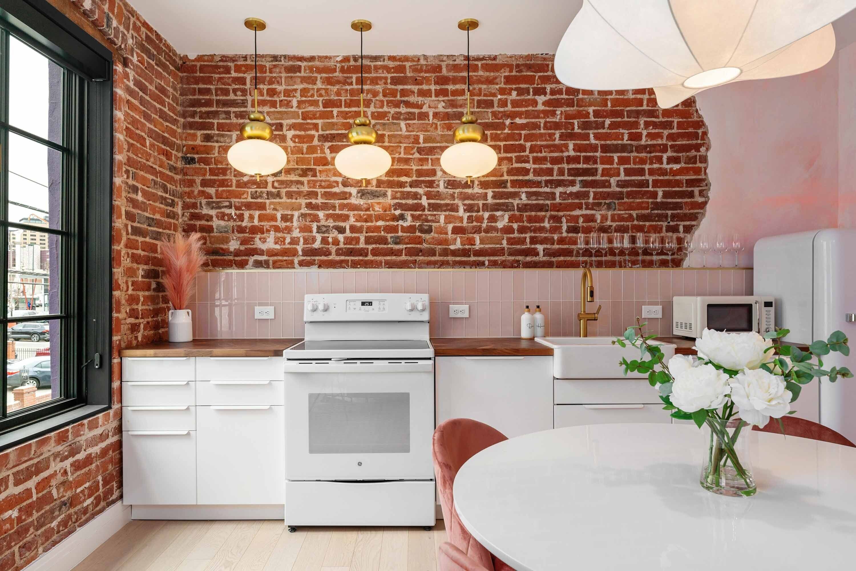 A kitchen with a brick wall, white appliances, and pendant lighting.