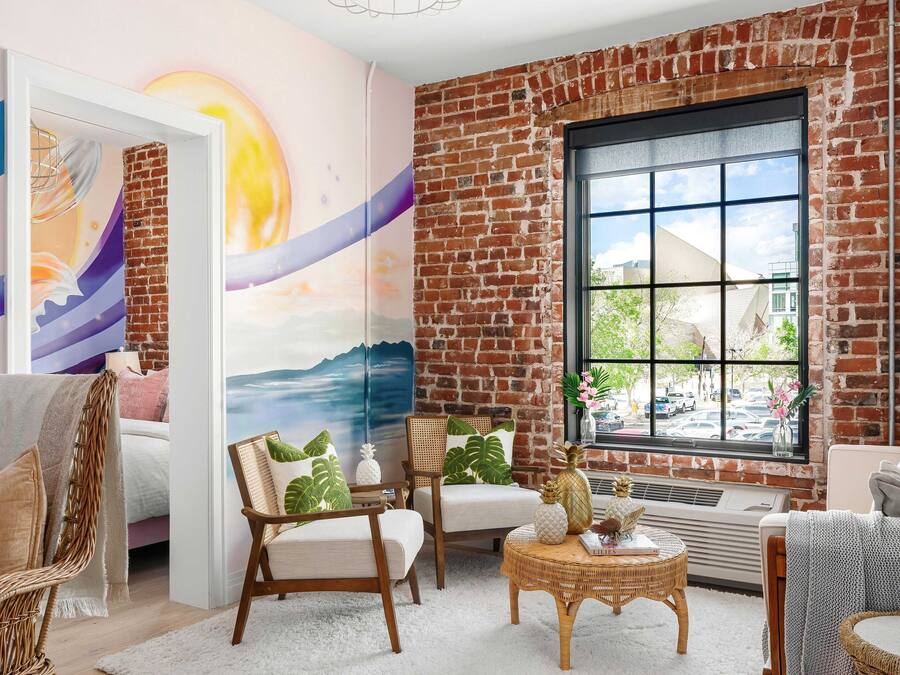 A cozy room with a brick wall, a large window, wicker furniture, and a mural on the wall.