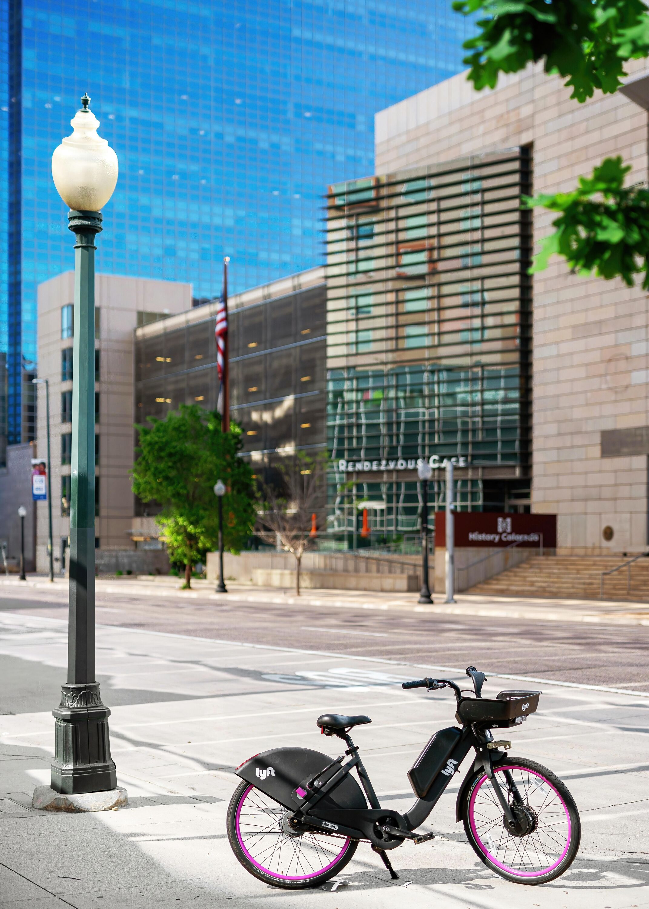 A stationary electric bike parked on a sidewalk next to a modern building with a glass facade.