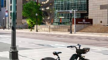 A stationary electric bike parked on a sidewalk next to a modern building with a glass facade.