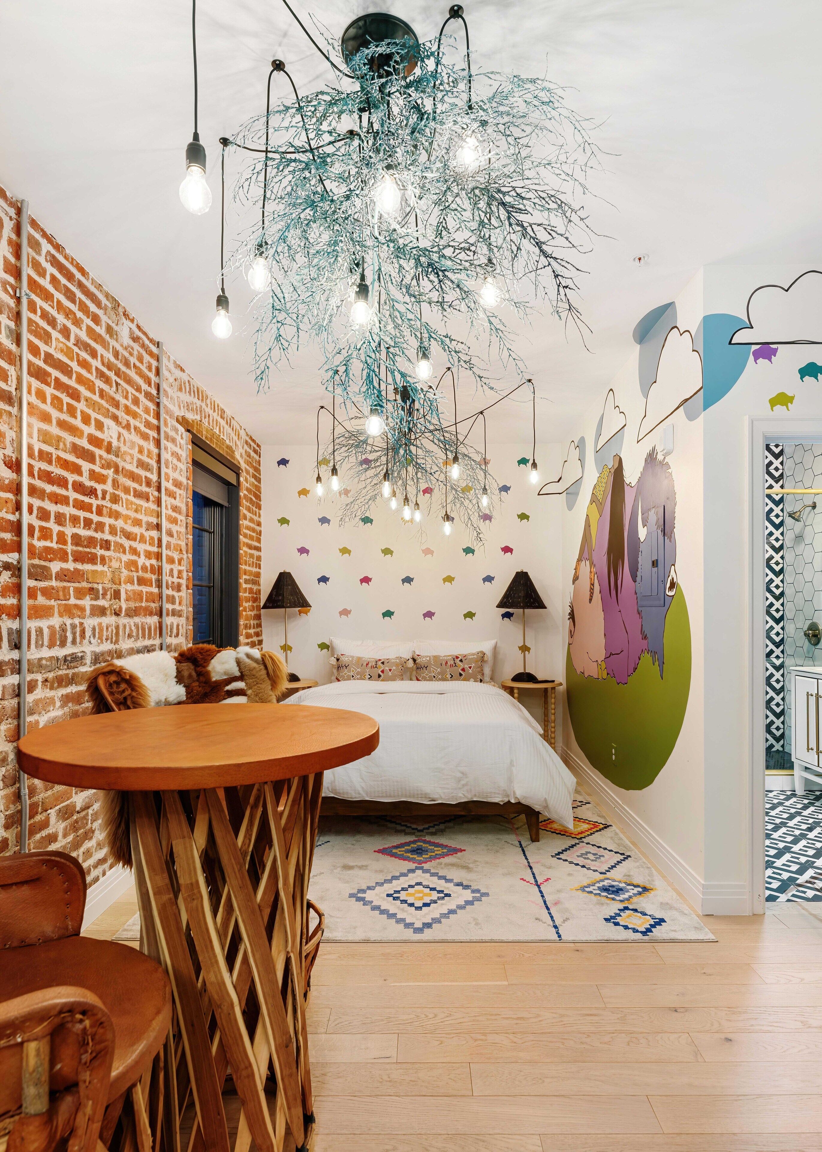 A cozy room with a brick wall, a bed with patterned pillows, a wooden table, and a unique ceiling light fixture.