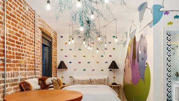 A cozy room with a brick wall, a bed with patterned pillows, a wooden table, and a unique ceiling light fixture.