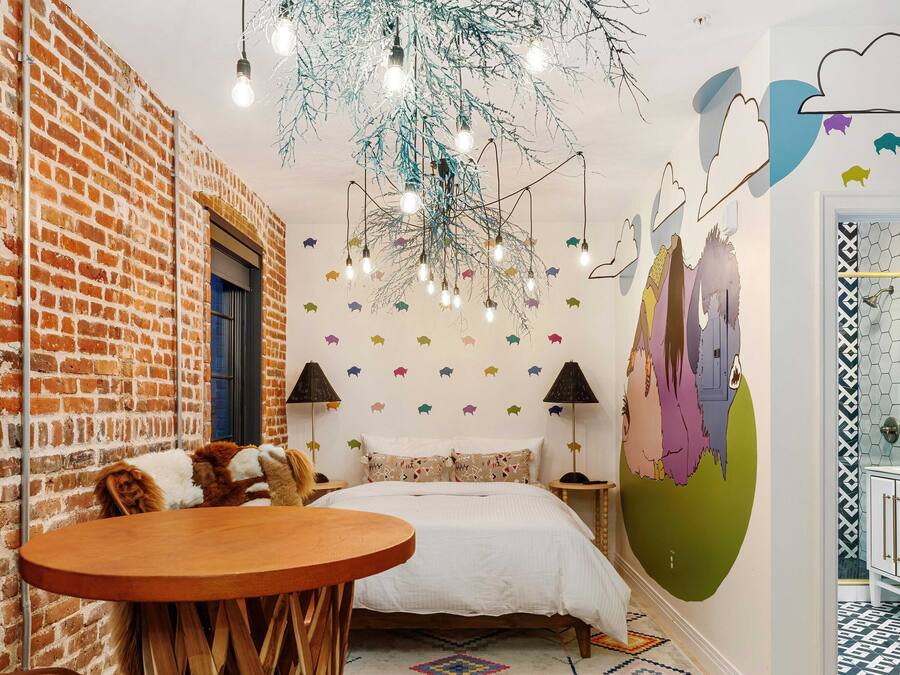 A cozy room with a brick wall, a bed with patterned pillows, a wooden table, and a unique ceiling light fixture.