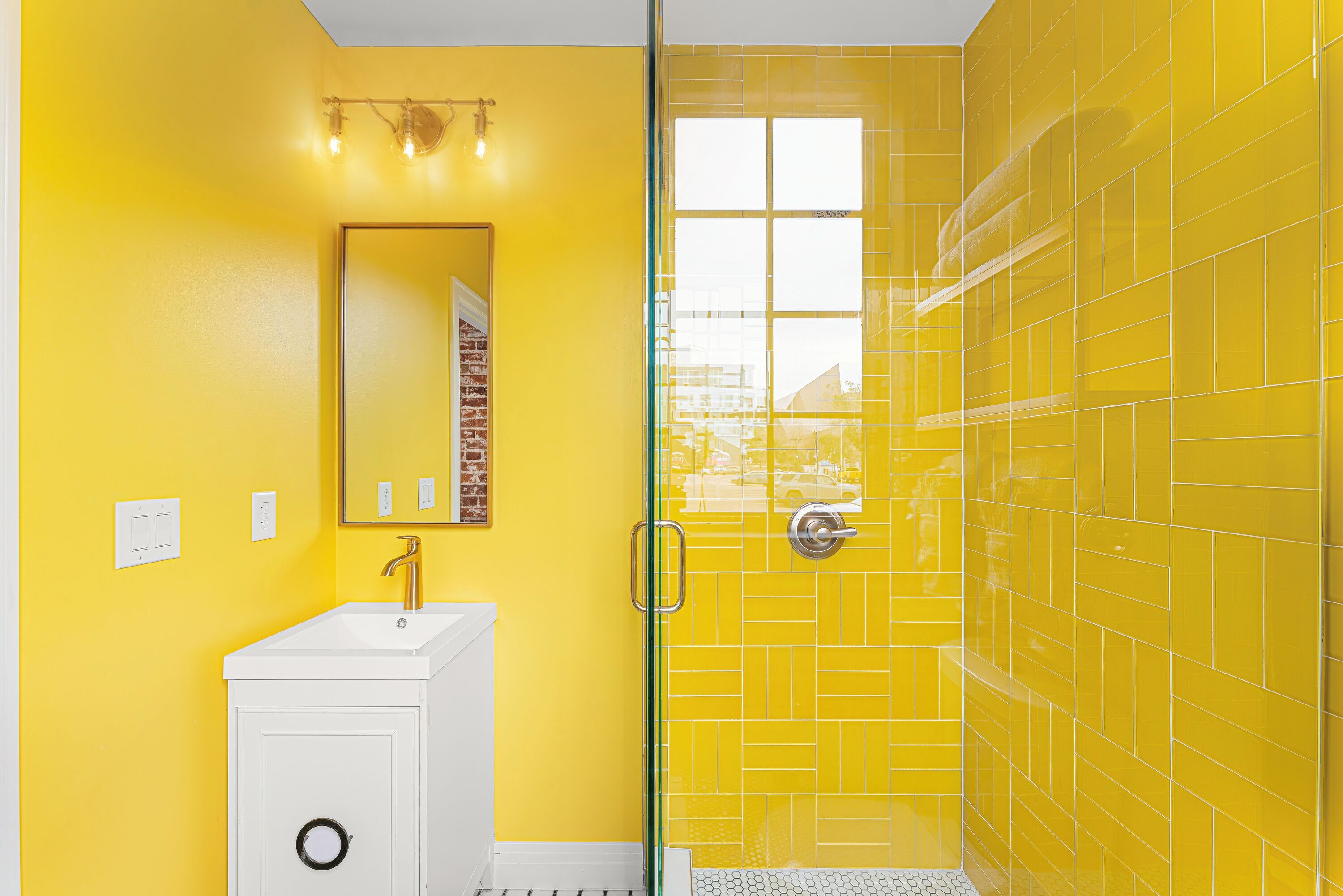 A bathroom with a white sink, a glass shower enclosure, and yellow walls.