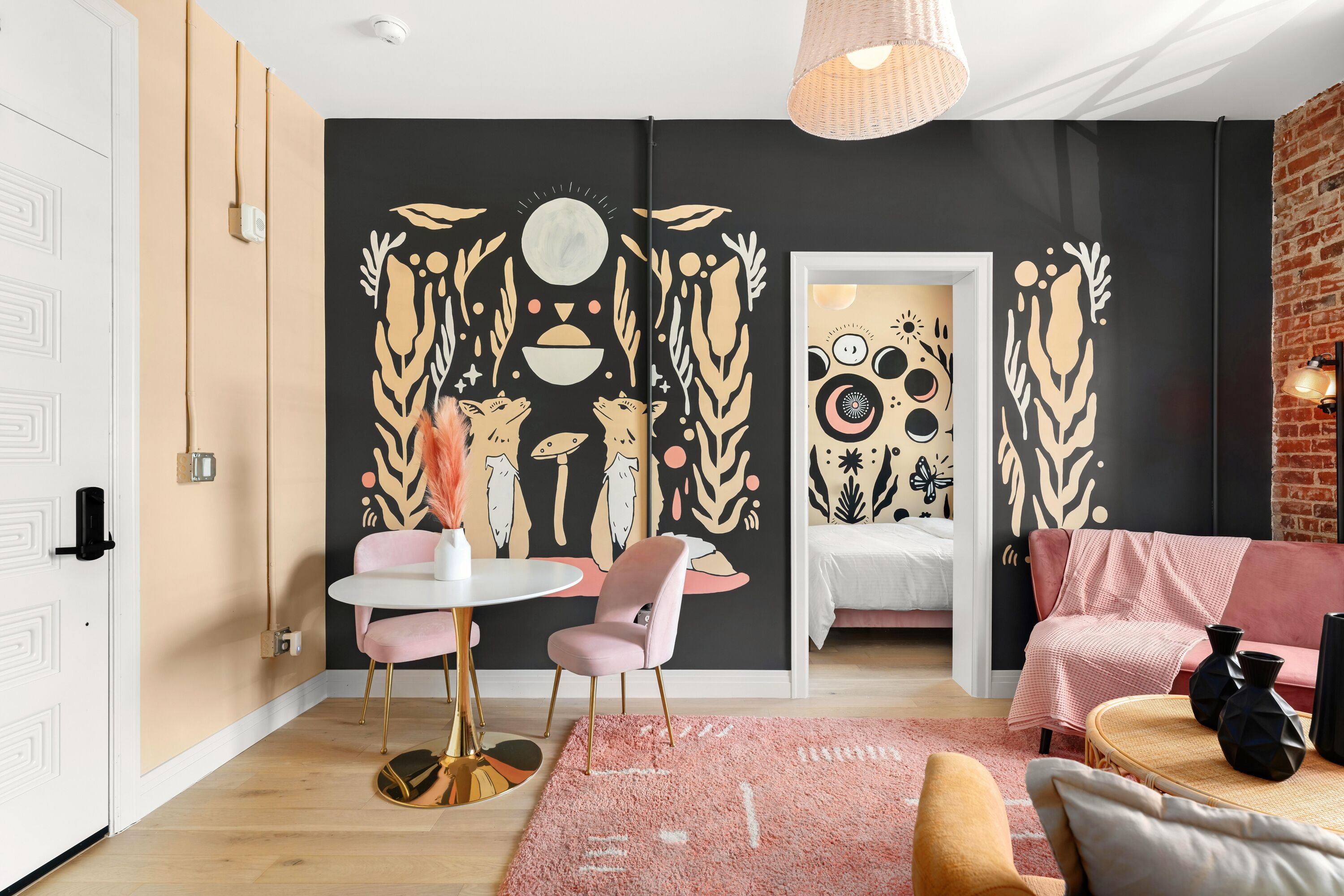 Uma sala de estar moderna com esquema de cores preto e bege, com uma mesa de jantar redonda com cadeiras cor de rosa, um sofá cor de rosa e um grande mural abstrato na parede.