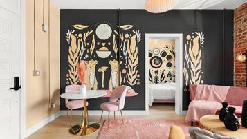 Uma sala de estar moderna com esquema de cores preto e bege, com uma mesa de jantar redonda com cadeiras cor de rosa, um sofá cor de rosa e um grande mural abstrato na parede.