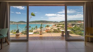 A room with a large sliding glass door leading to a balcony with a view of the ocean and hills. - Maravilhosa Mansão em Frente à Praia (Búzios)