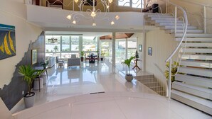 A spacious interior with a modern staircase, a chandelier, and a view of the outdoors. - Maravilhosa Mansão em Frente à Praia (Búzios)