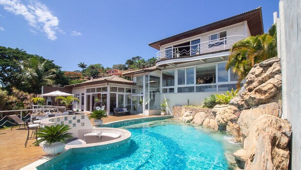 A modern house with a swimming pool, outdoor seating, and a view of the surrounding landscape. - Maravilhosa Mansão em Frente à Praia (Búzios)