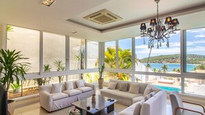 A spacious living room with large windows, a chandelier, and a view of the ocean. - Maravilhosa Mansão em Frente à Praia (Búzios)
