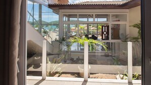 A modern house with large glass windows, a balcony with potted plants, and a view of a coastal area. - Maravilhosa Mansão em Frente à Praia (Búzios)