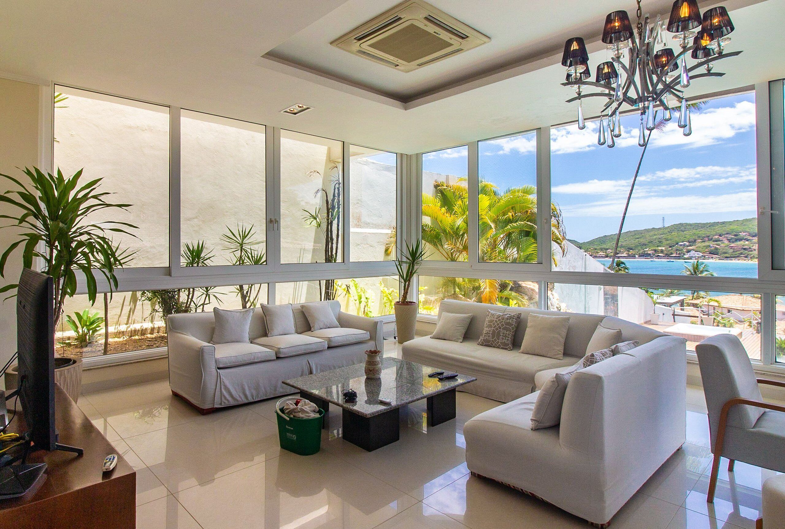 A spacious living room with large windows, white sofas, a coffee table, and a chandelier.