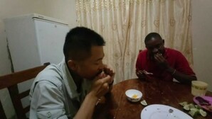 Two people sitting at a wooden table with a white plate and a bowl of food. - Kinyaiya's Farm Lodge (Moshi)