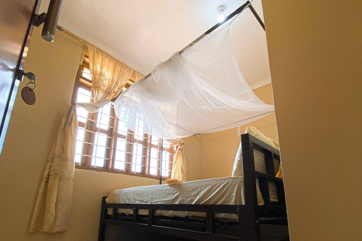 A room with a bed under a mosquito net, a window with curtains, and a tiled floor.